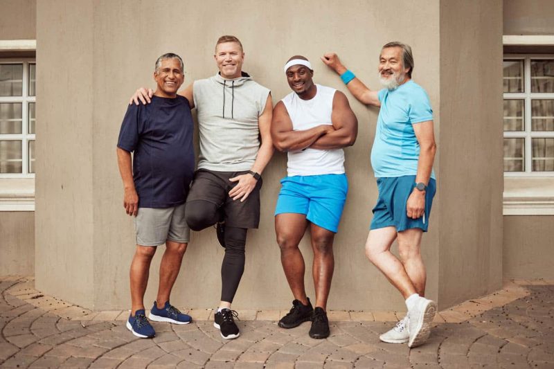 Happy men, fitness portrait and group exercise on wall background in urban city. Smile, sports trai.